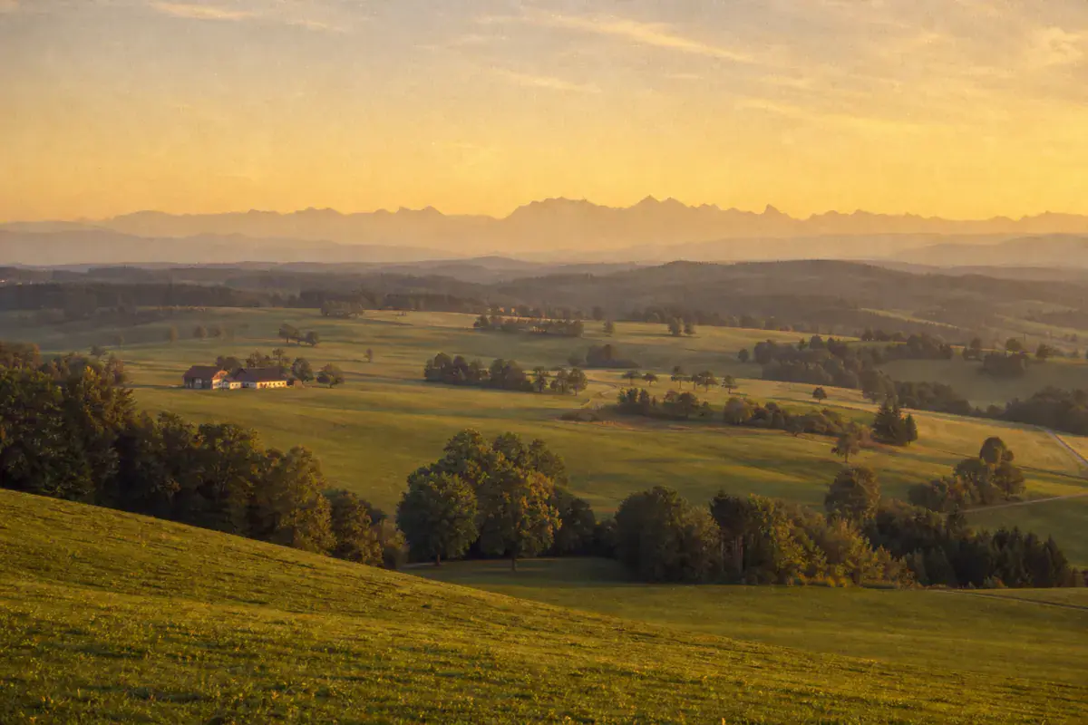 Weite oberbayerische Voralpenlandschaft im Abendlicht mit den Alpen am Horizont